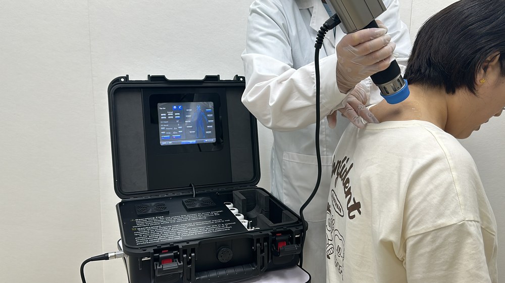 Operator applying the applicator head to a patient's shoulder over coupling gel, gloved hand steadying the neck