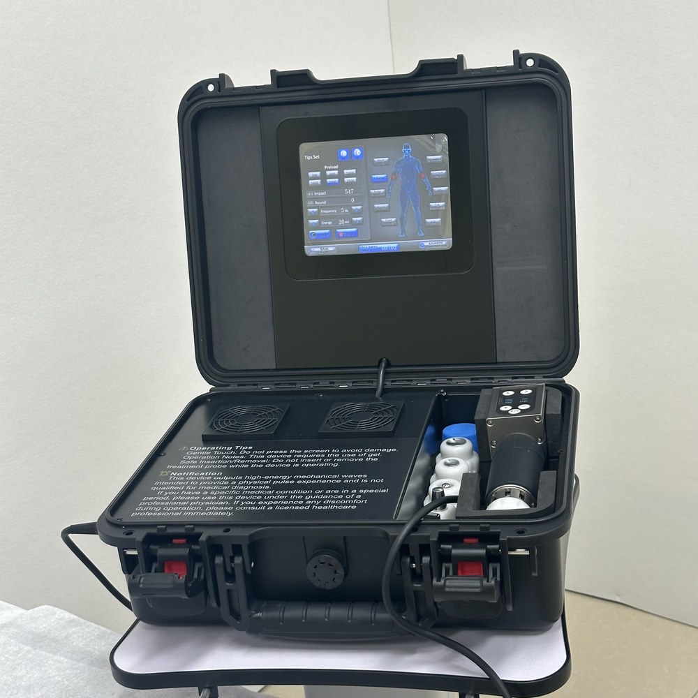 Portable shockwave unit with the handpiece seated in its cradle, spare heads racked alongside and the printed operating tips visible on the case interior