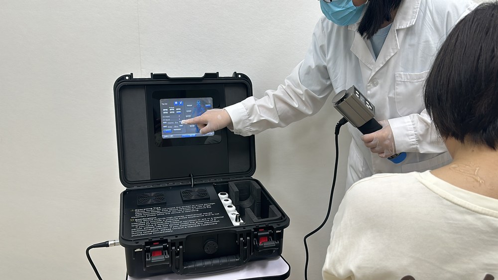 Operator selecting a treatment preset on the portable shockwave unit while holding the applicator