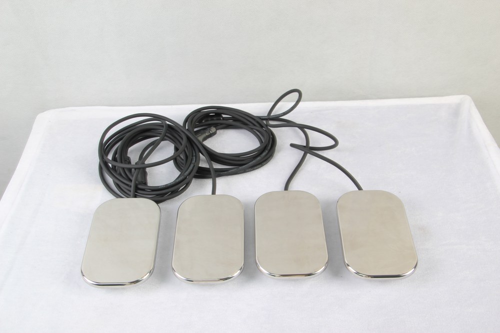 Four stainless steel TECAR electrode plates with their cables laid out on a treatment couch